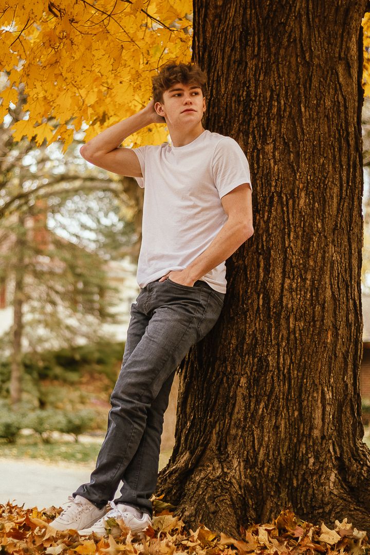 Four sequential shots of someone in a white t-shirt and gray pants leaning against a tree trunk with golden autumn leaves.
