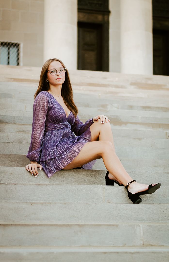 Someone in a purple lace dress sits elegantly on concrete stairs while wearing black heels.