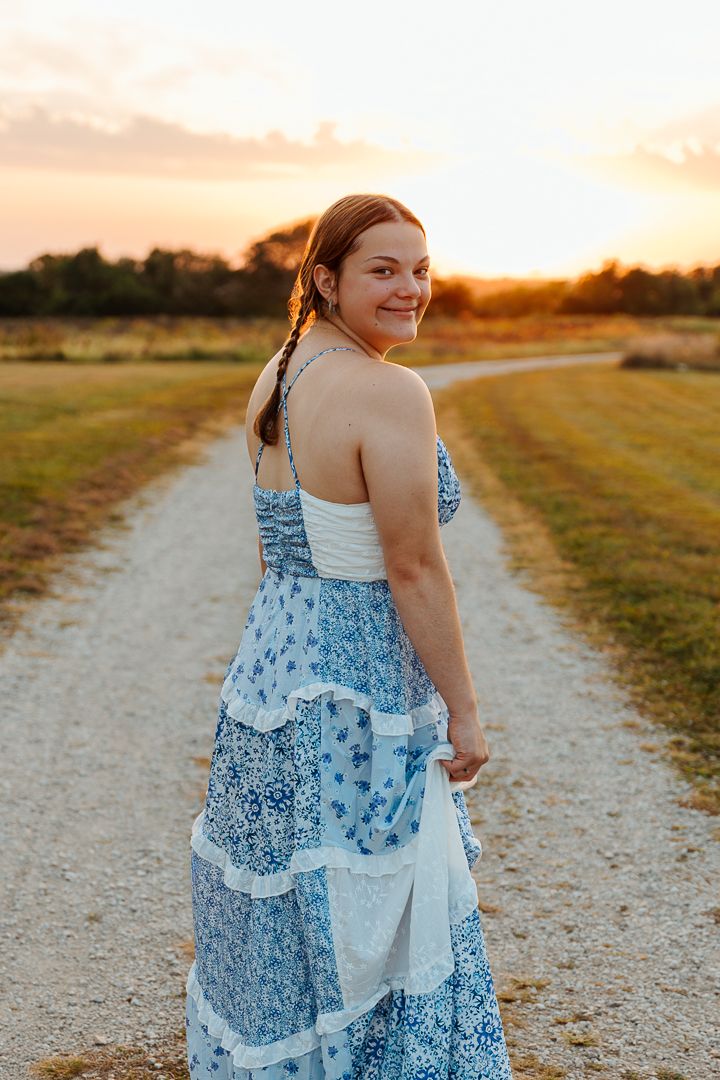 A sunny golden hour portrait of someone in a blue and white floral tiered maxi dress on a dirt path at sunset.