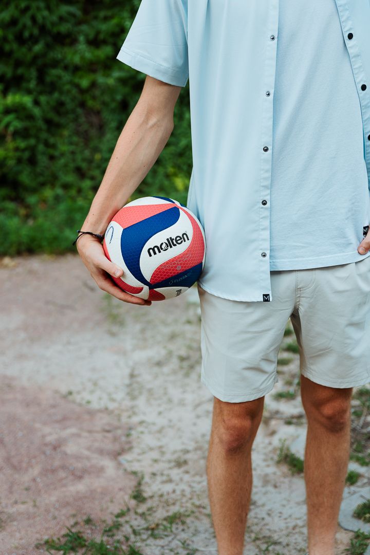 Three partial views of someone wearing a blue shirt and shorts posing with a volleyball against a wooded background.