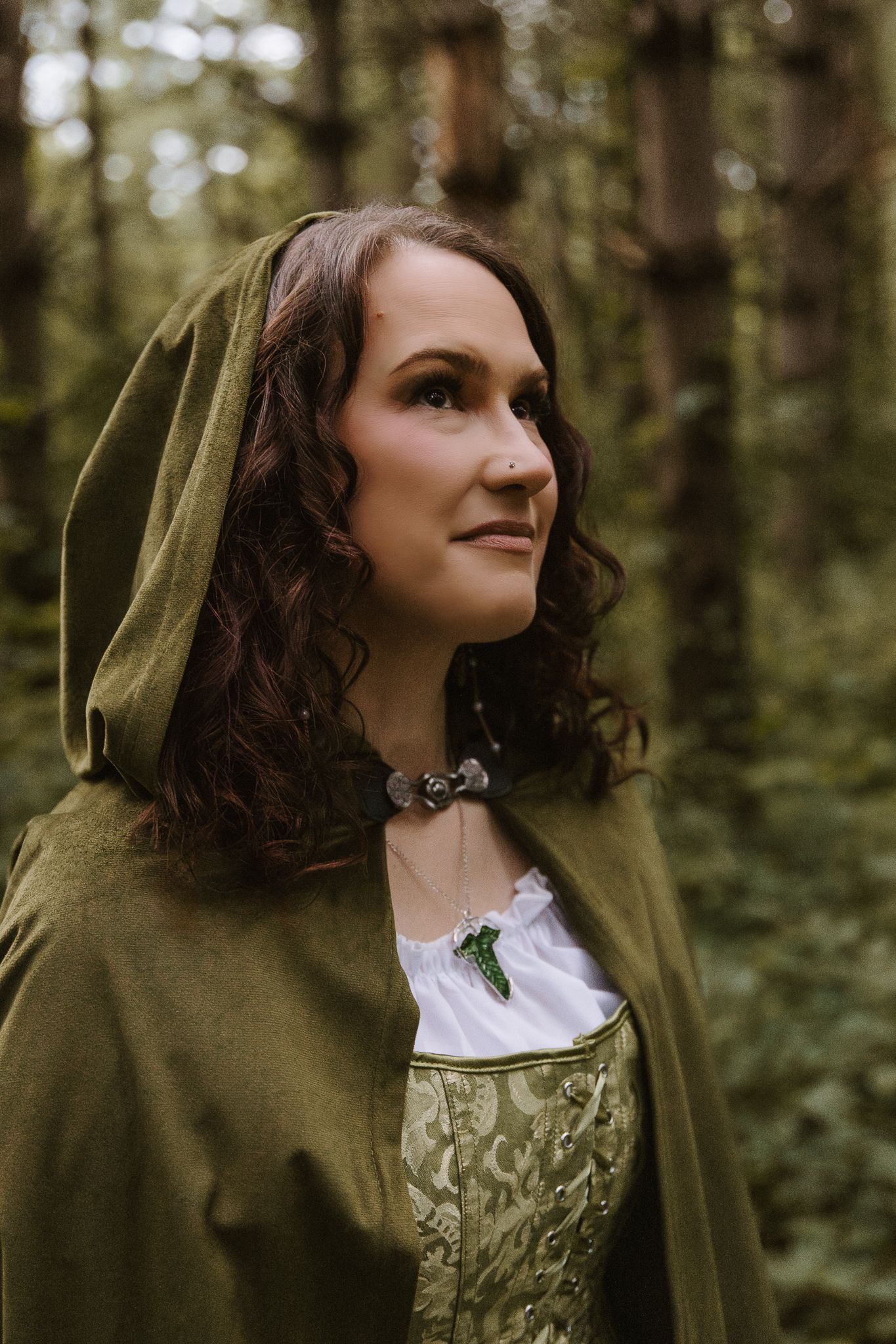 Woman wearing a green hooded cloak and white dress smiling in a forest.