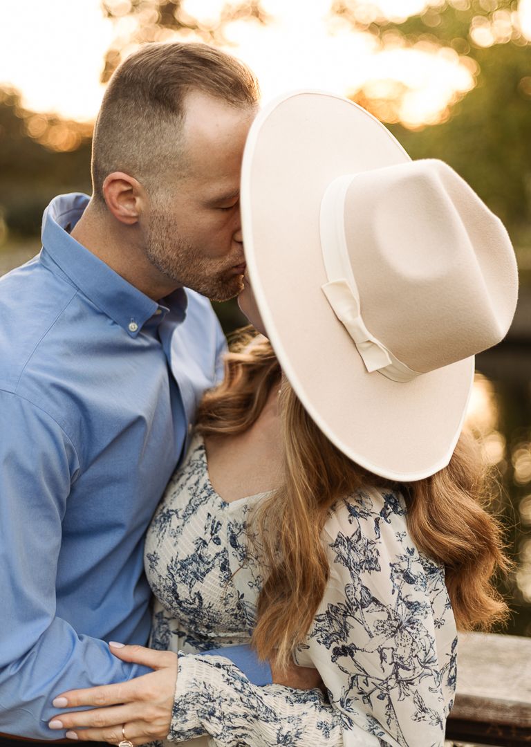 A romantic couple in western attire share tender moments at sunset while wearing a cowboy hat and blue shirt.