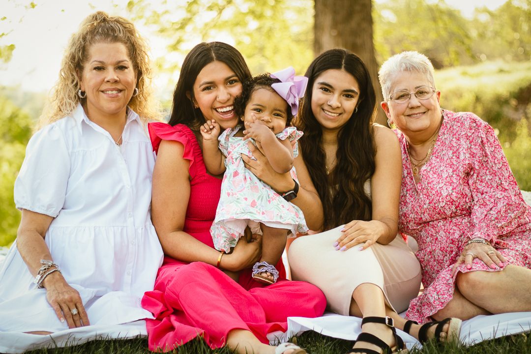 Multi-generational family enjoying a sunny day outdoors while sitting together on grass in casual attire.