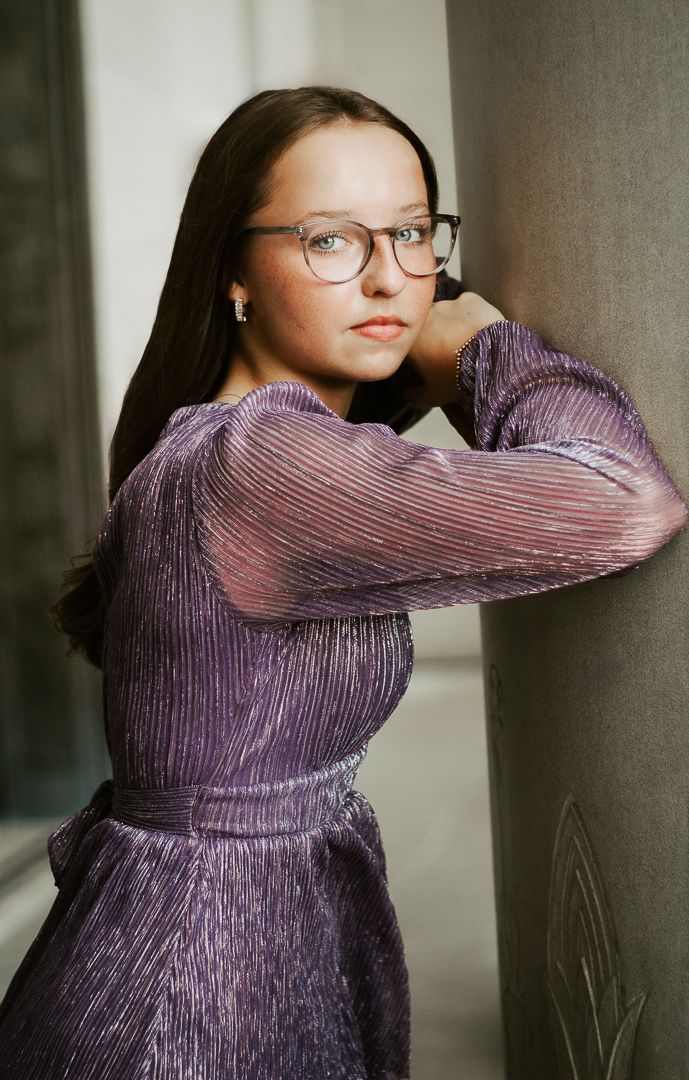 Person in a shimmering purple dress poses gracefully against a neutral background in artistic photoshoot series.