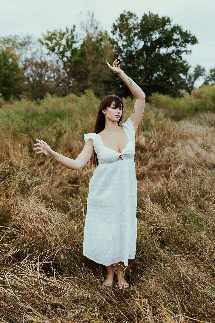 Woman in flowing white dress dances gracefully through tall golden grass in a meadow.