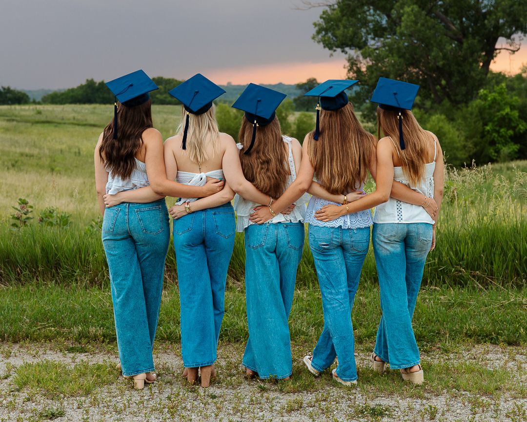 Group of graduates in turquoise scrubs pose together with their backs to camera at sunset in a grassy field.