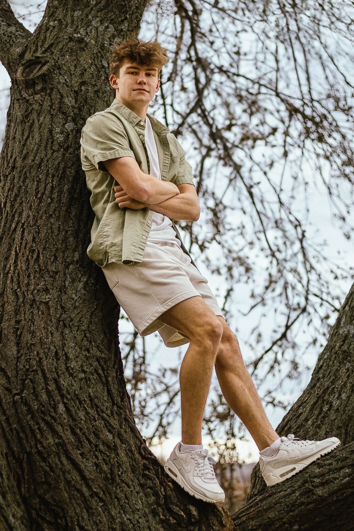 Child's feet in white sneakers balanced on a large tree branch against a backdrop of bare winter branches.