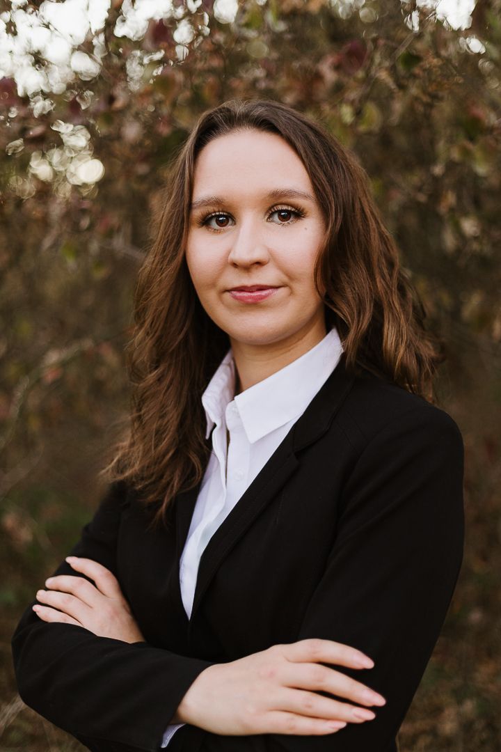 Professional portrait in black blazer and white shirt against autumn foliage background.