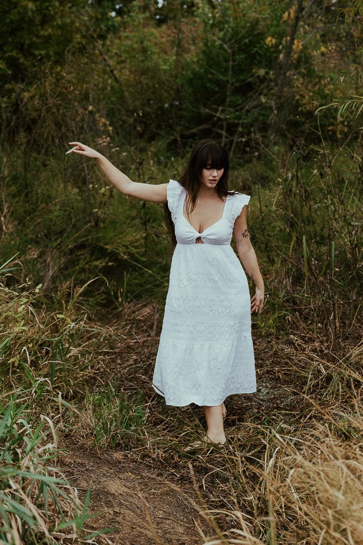 White dress flows through wild grass and greenery in an artistic outdoor photoshoot.