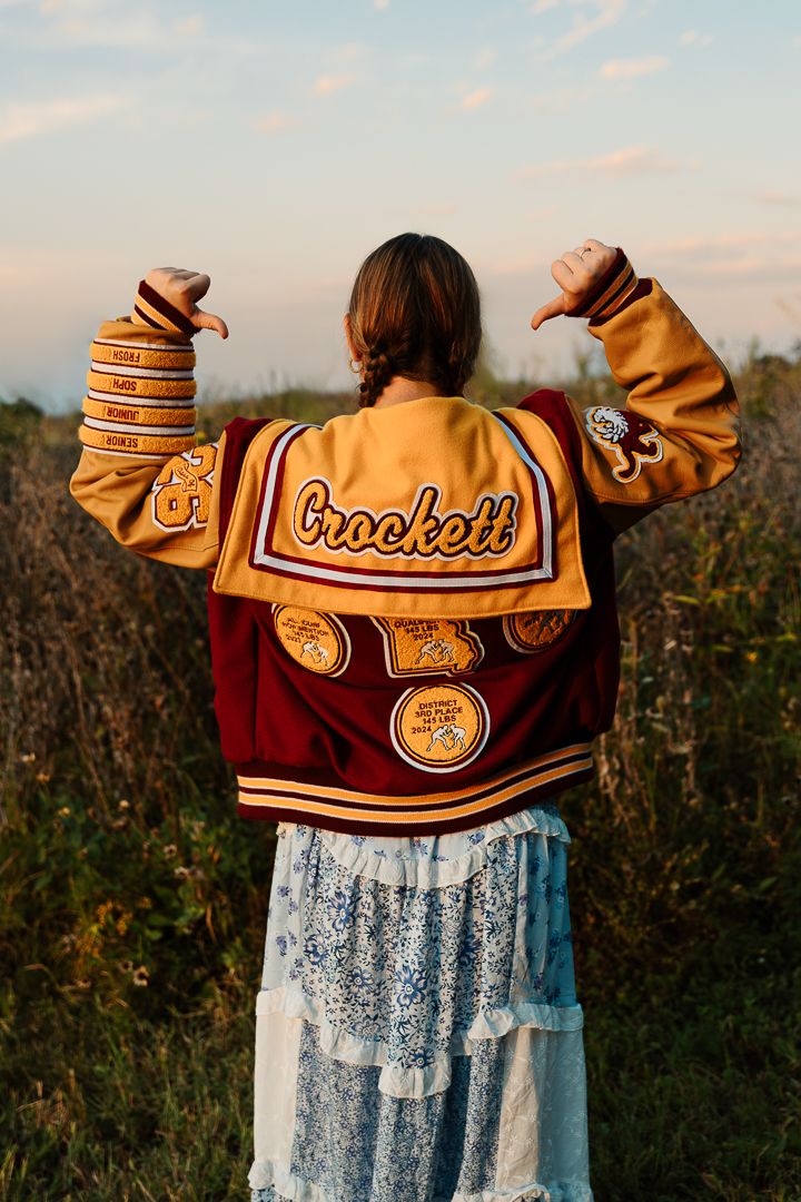 Back view of a maroon and gold varsity jacket paired with a floral dress in an outdoor setting.