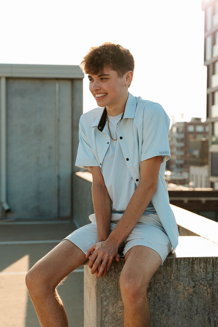 Young person in white polo shirt sitting outdoors and smiling during golden hour.