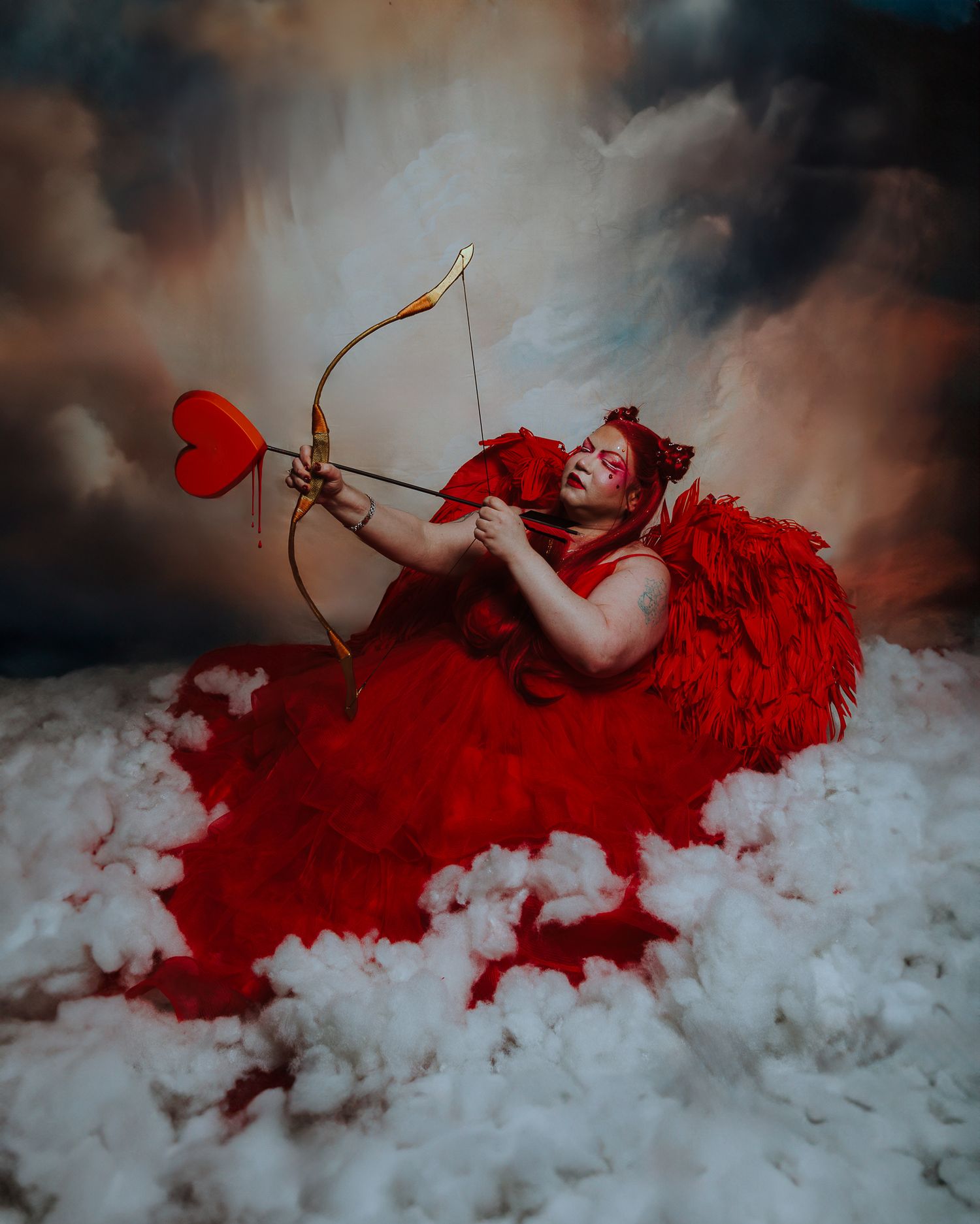 A plus-size Cupid in a red feathered gown aims a heart-tipped arrow while sitting on clouds against a dramatic sky.
