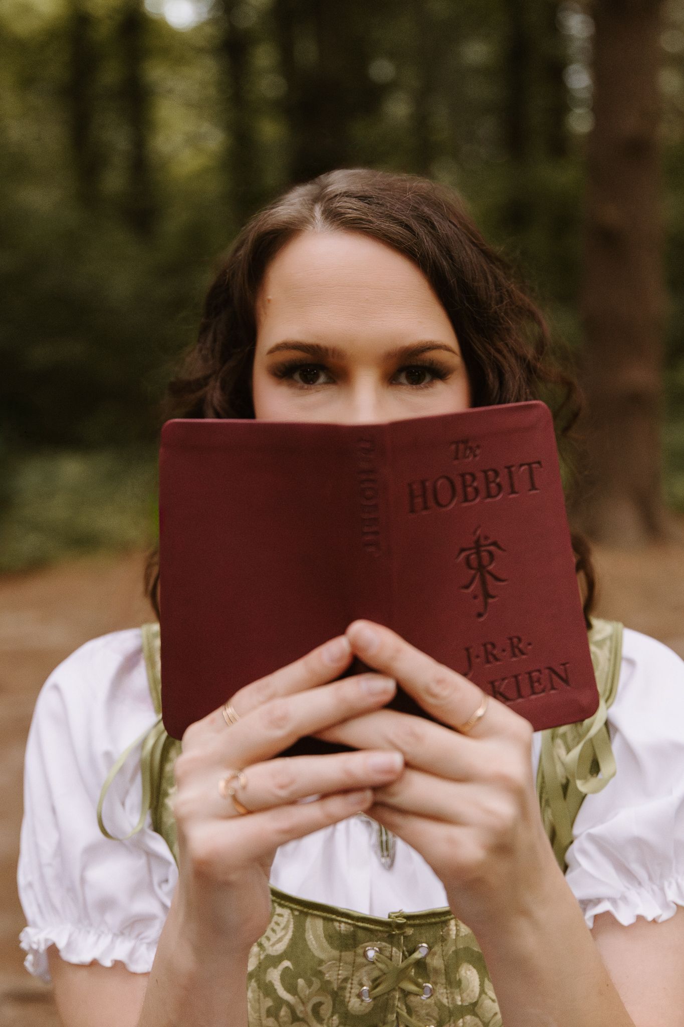 Woman holding a red copy of The Hobbit by J.R.R. Tolkien in a forest.