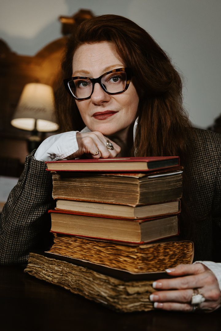 A collection of vintage books and reading glasses arranged in moody lighting on a dark textured surface.