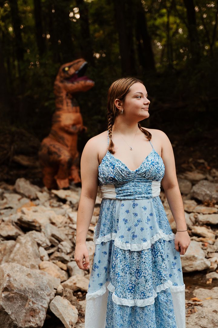 Person wearing a blue floral summer dress poses on rocky terrain in a woodland setting.