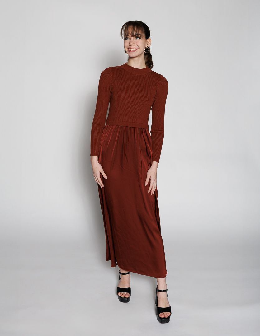 Woman wearing a rust brown long sleeve maxi dress with gathered waist and black heeled sandals.