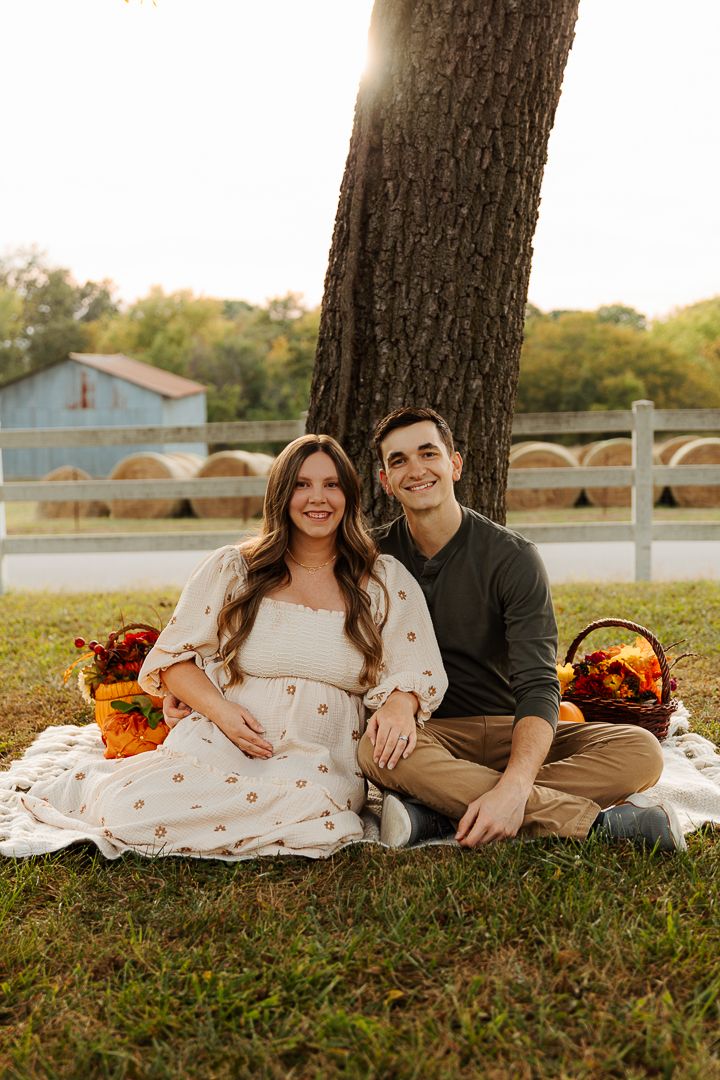 Couple lounges on grass with autumn decorations and pumpkins during outdoor photo session.