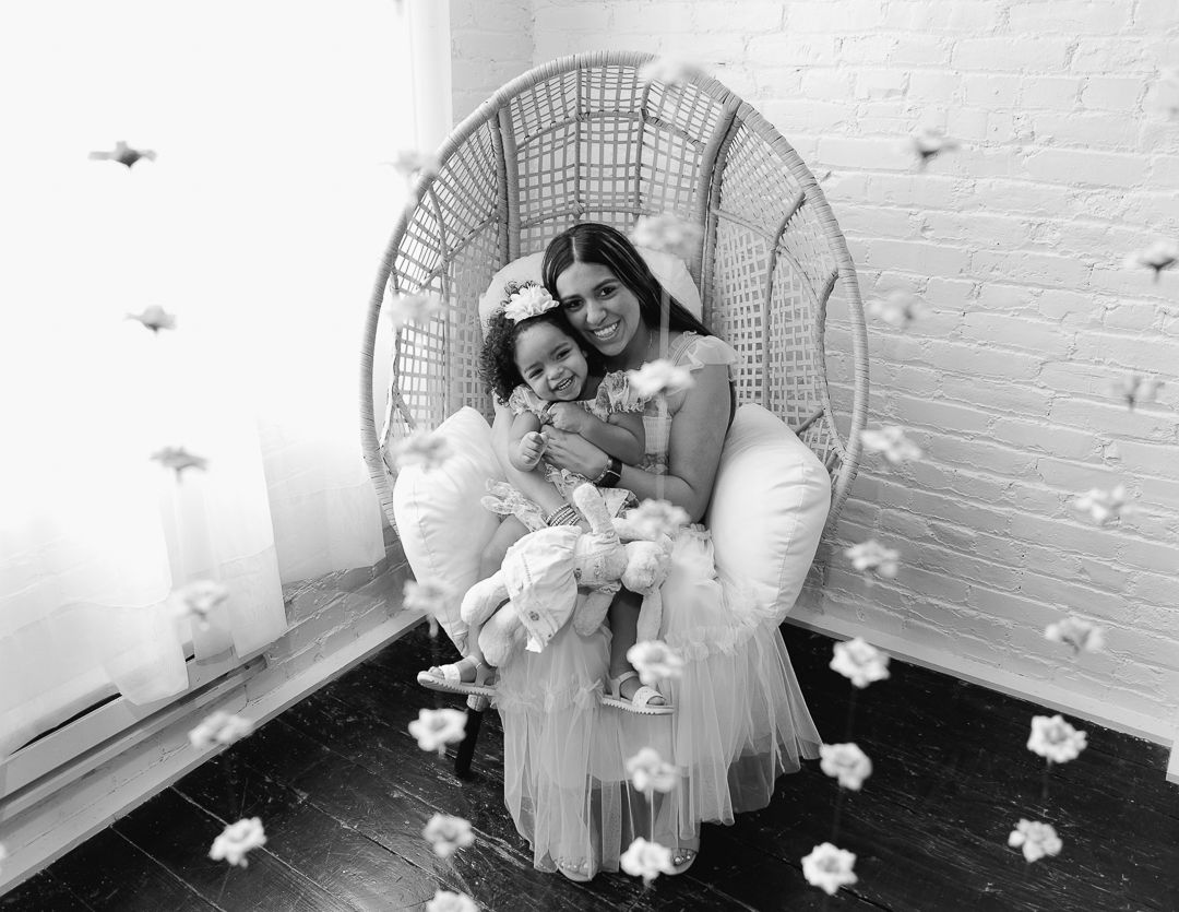 A black and white photo series showing intimate moments of a couple relaxing in a papasan chair with white flowers.