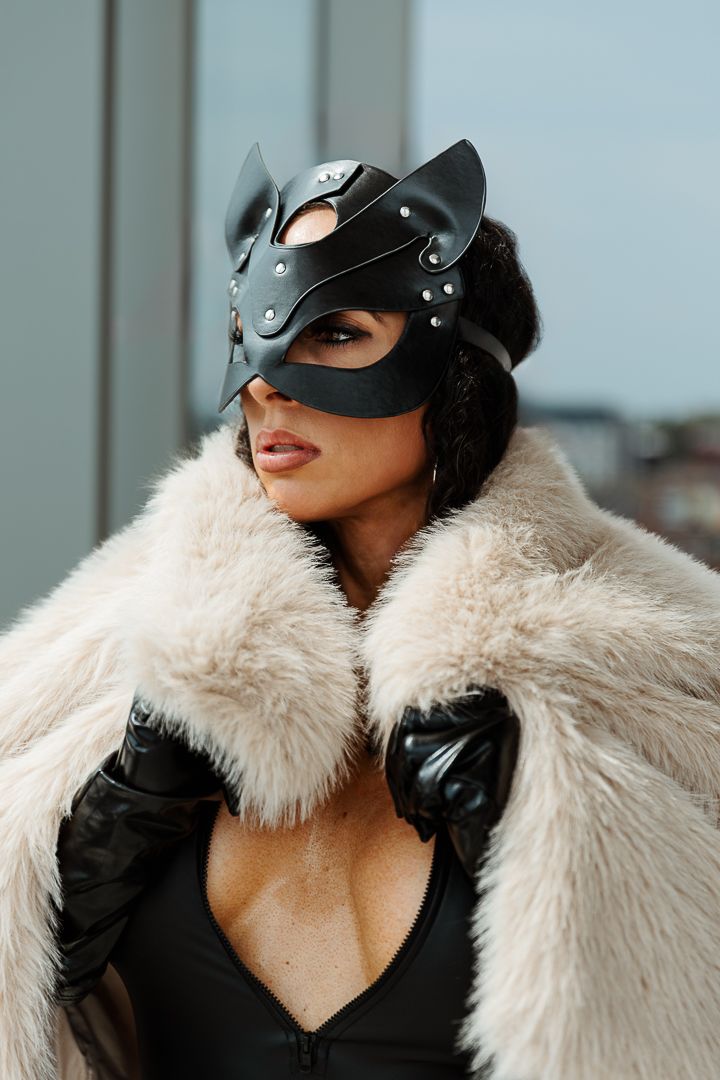 A stylish model in a white fur coat, black gloves, and helmet visor poses against a light background.
