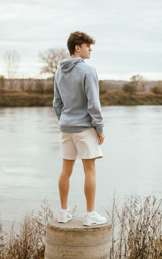 Someone wearing a grey sweatshirt and white shorts stands on a concrete pillar overlooking a serene lake.