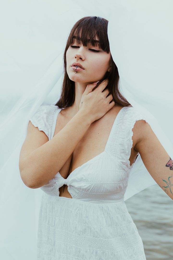 Close-up portrait of woman in white lace dress against light background.