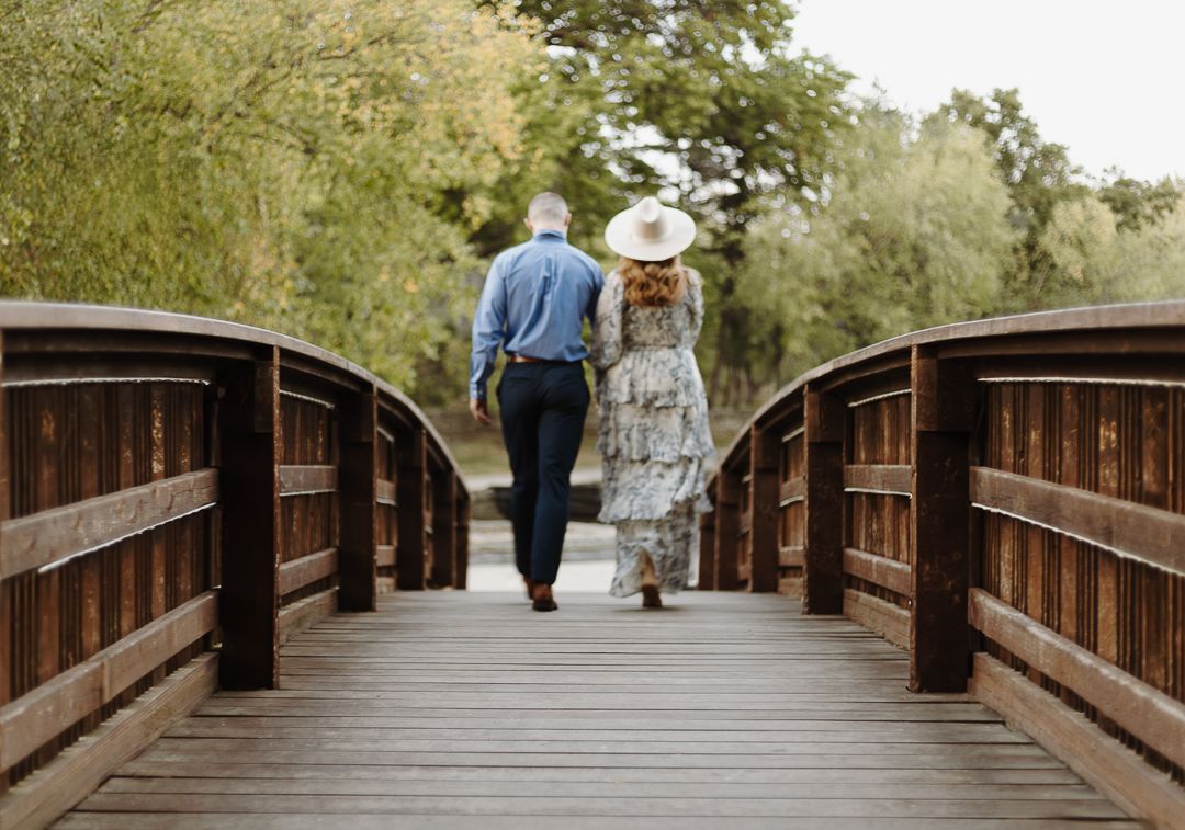 Walking path on wooden bridge through tree-lined trail with distant walkers in a peaceful natural setting.