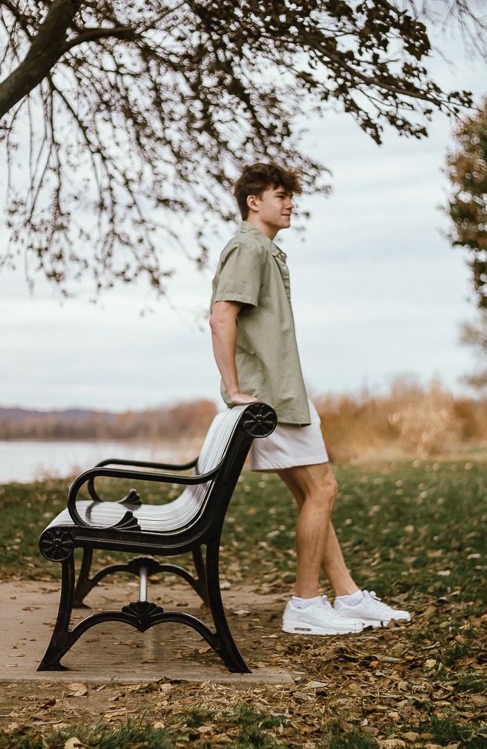 Park bench on fallen autumn leaves photographed at different angles with figure in khaki shirt and white shoes.