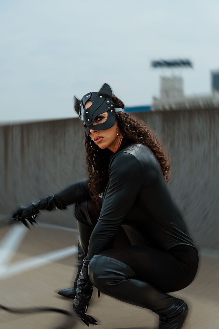 Person in a black catsuit and mask crouches on a rooftop in a dramatic superhero-inspired pose.