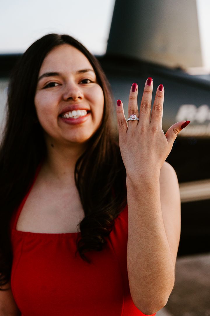 A woman in a red dress shows off her engagement ring with a bright smile.