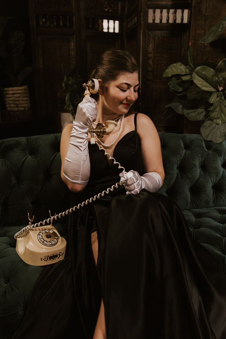 A vintage rotary telephone sits on a dark velvet couch while someone reaches to answer an incoming call.