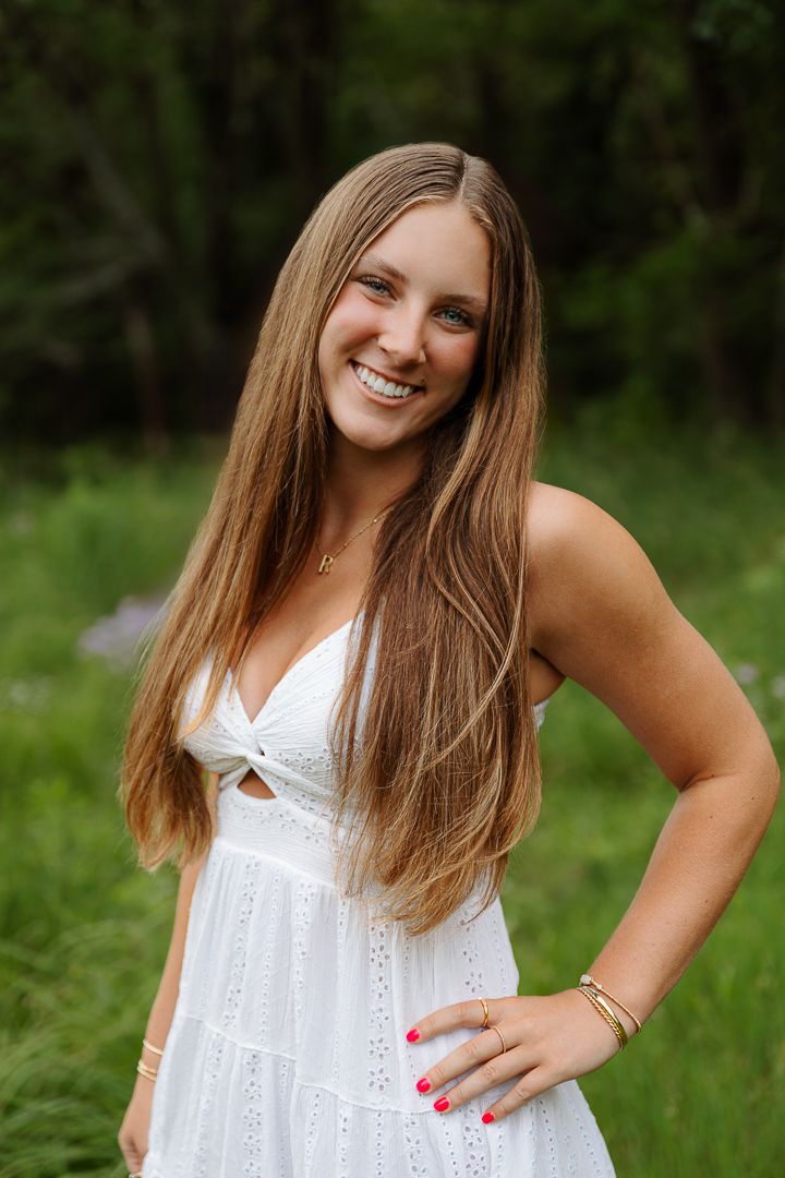 Person in white eyelet dress poses against green natural background.