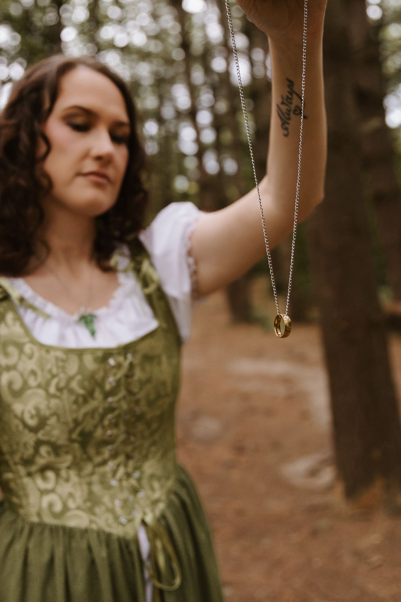 Woman in green renaissance dress holds One Ring necklace in forest, LOTR cosplay photoshoot.