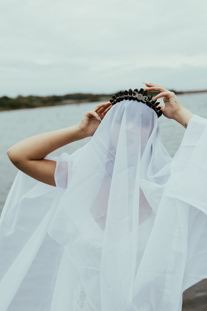 Hands holding and adjusting a delicate white veil against cloudy sky.