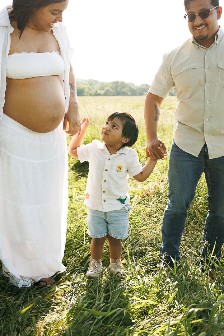 A family dressed in white stands together in a sunlit meadow during a golden hour photo session.
