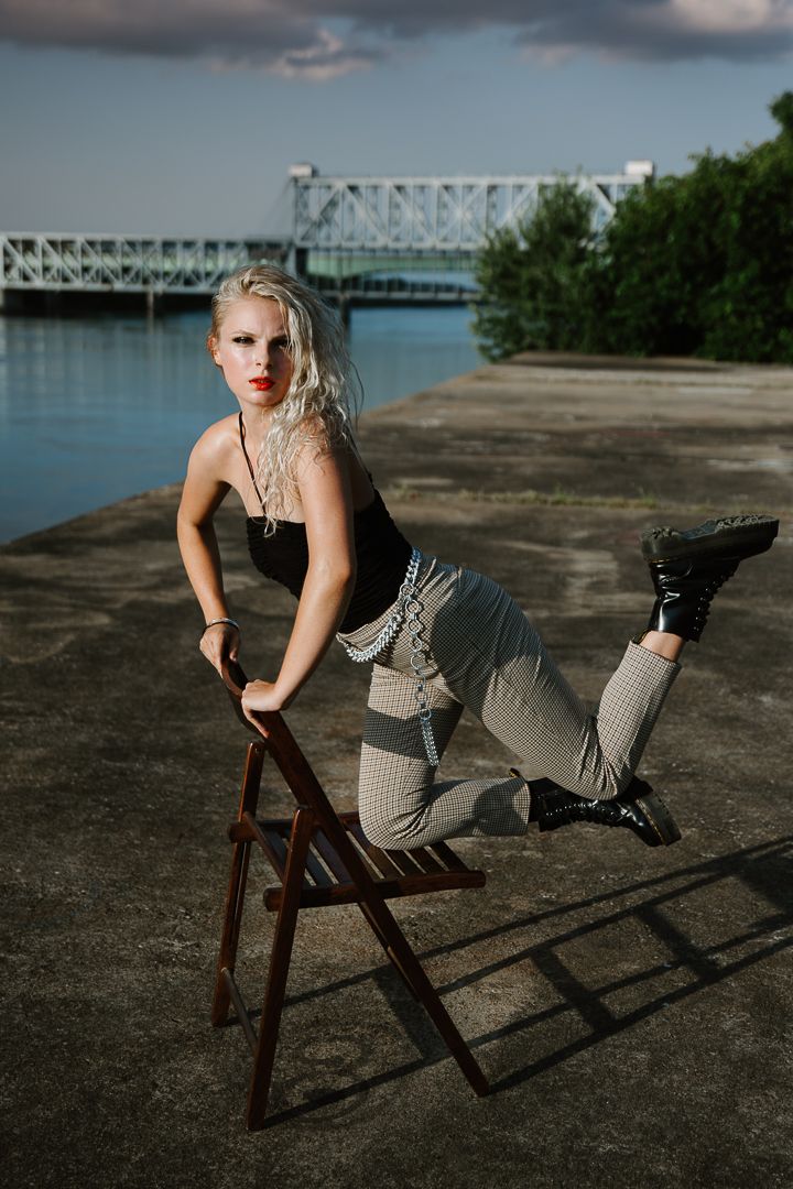 Artistic portrait session featuring dynamic poses on a chair with industrial bridge backdrop.