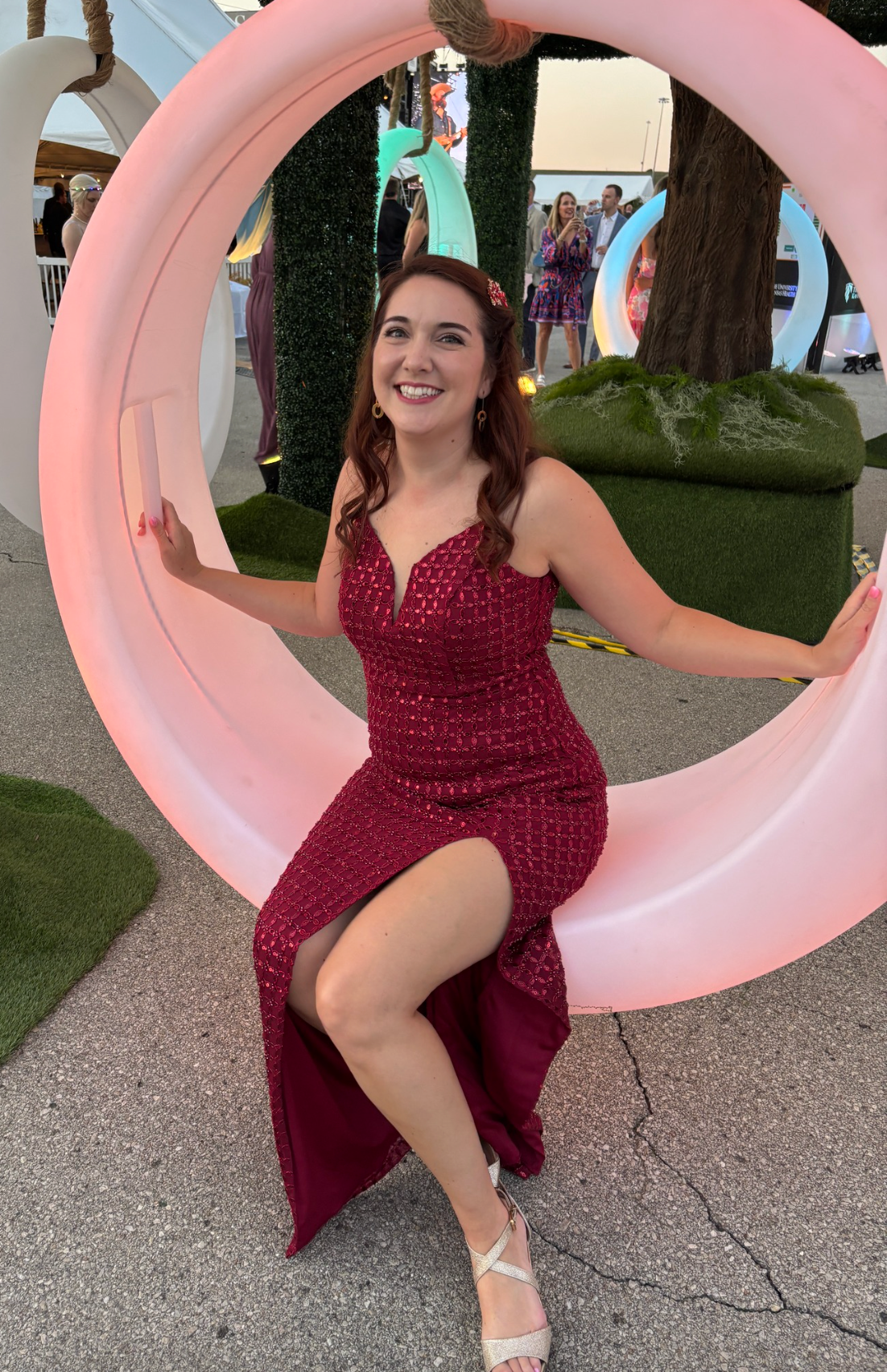 A person in a burgundy polka dot dress poses playfully with a large pink circular art installation outdoors.