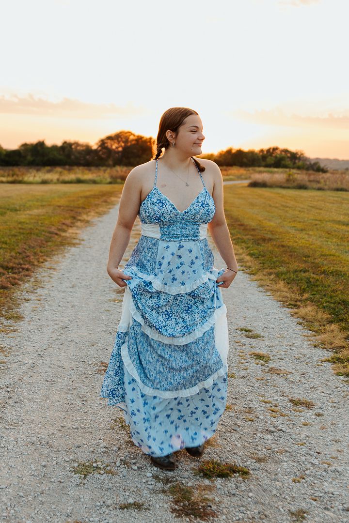 A flowing blue and white floral maxi dress stands out against a sunset-lit country path.