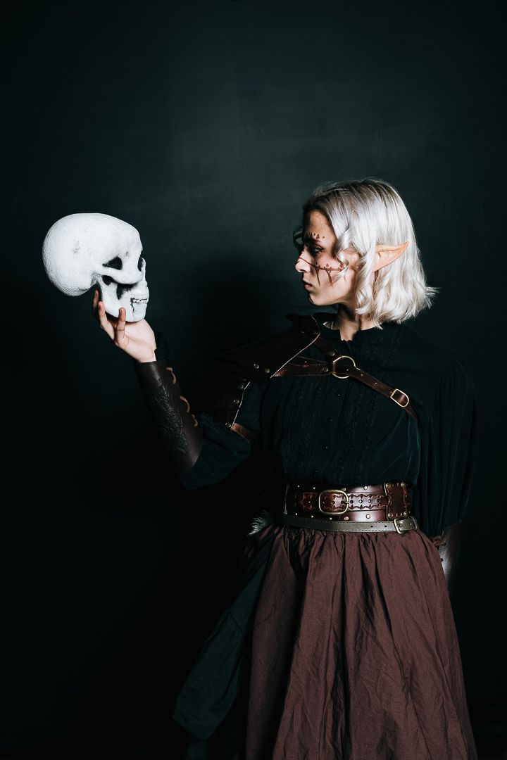 A figure in a dark dress and white mask poses dramatically against a black background in a series of artistic shots.