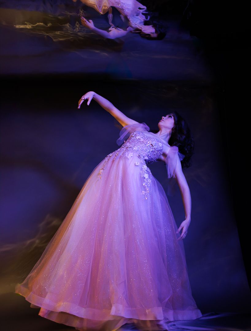 Dancer in flowing pink gown creates ethereal movement against purple backdrop.