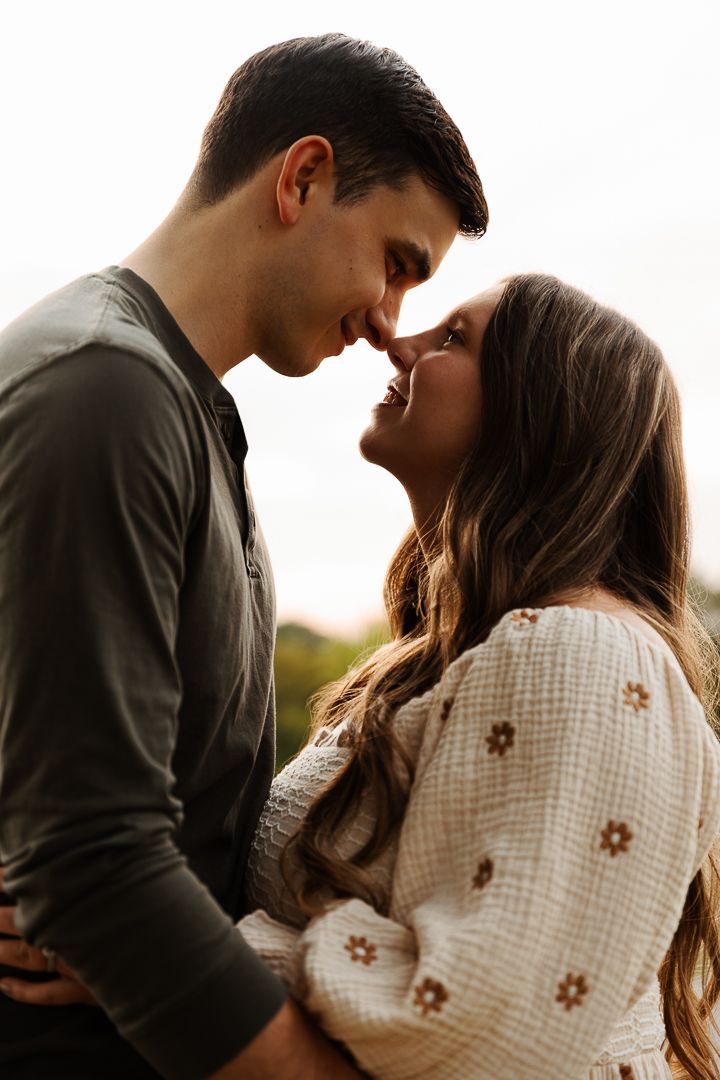 A romantic couple in intimate pose sharing a tender moment at sunset in casual attire.