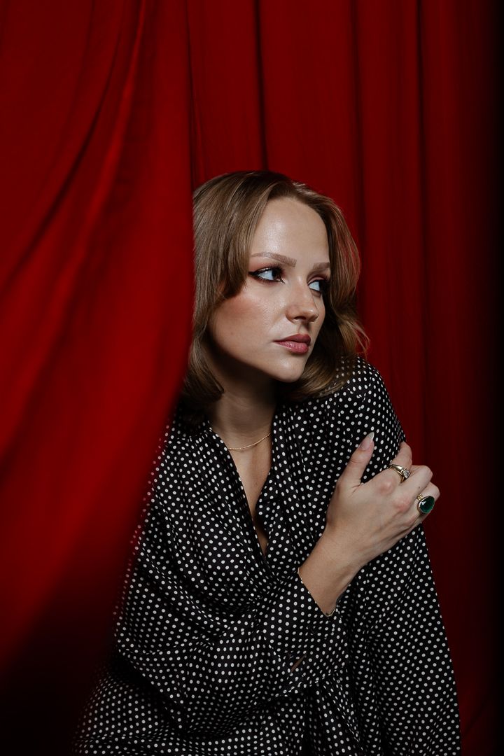 Dramatic portrait with polka dot outfit against red velvet curtain backdrop.