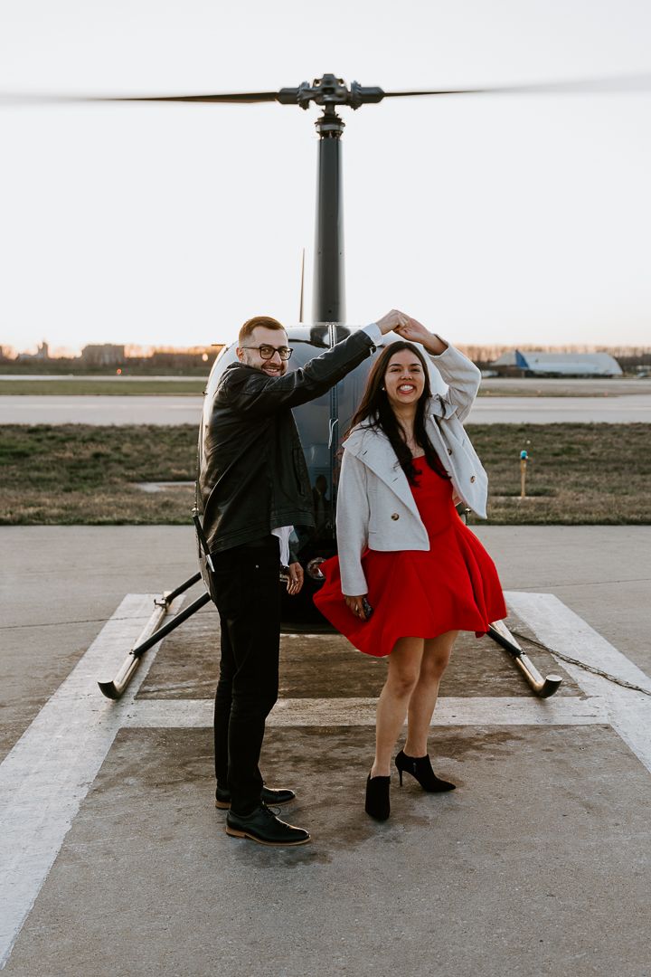Couple in romantic poses by an aircraft propeller during an outdoor photoshoot at an airfield.