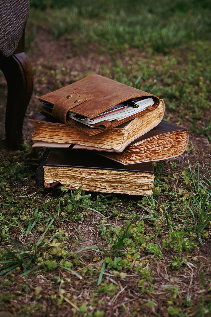 Old worn leather books with yellowed pages lay scattered on grass in an artistic arrangement.