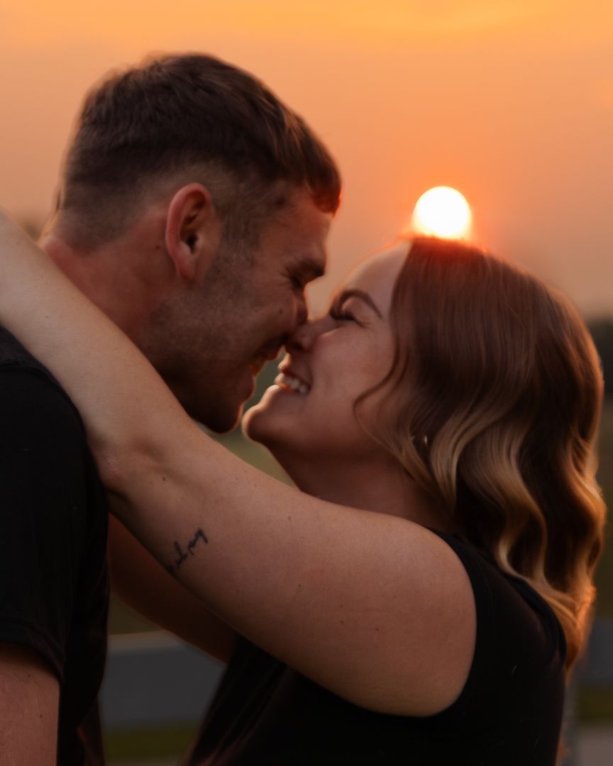 Two people embrace passionately during a golden sunset near a wooden fence.