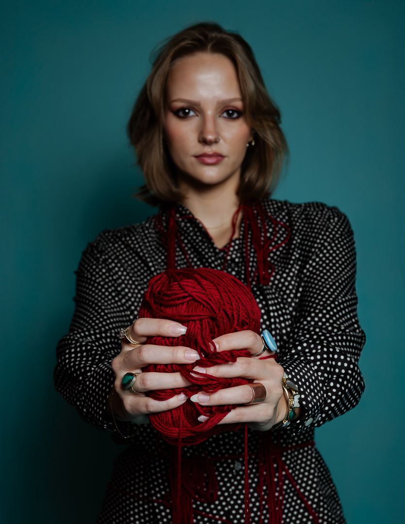 Stylized photo with model holding red yarn against teal background.