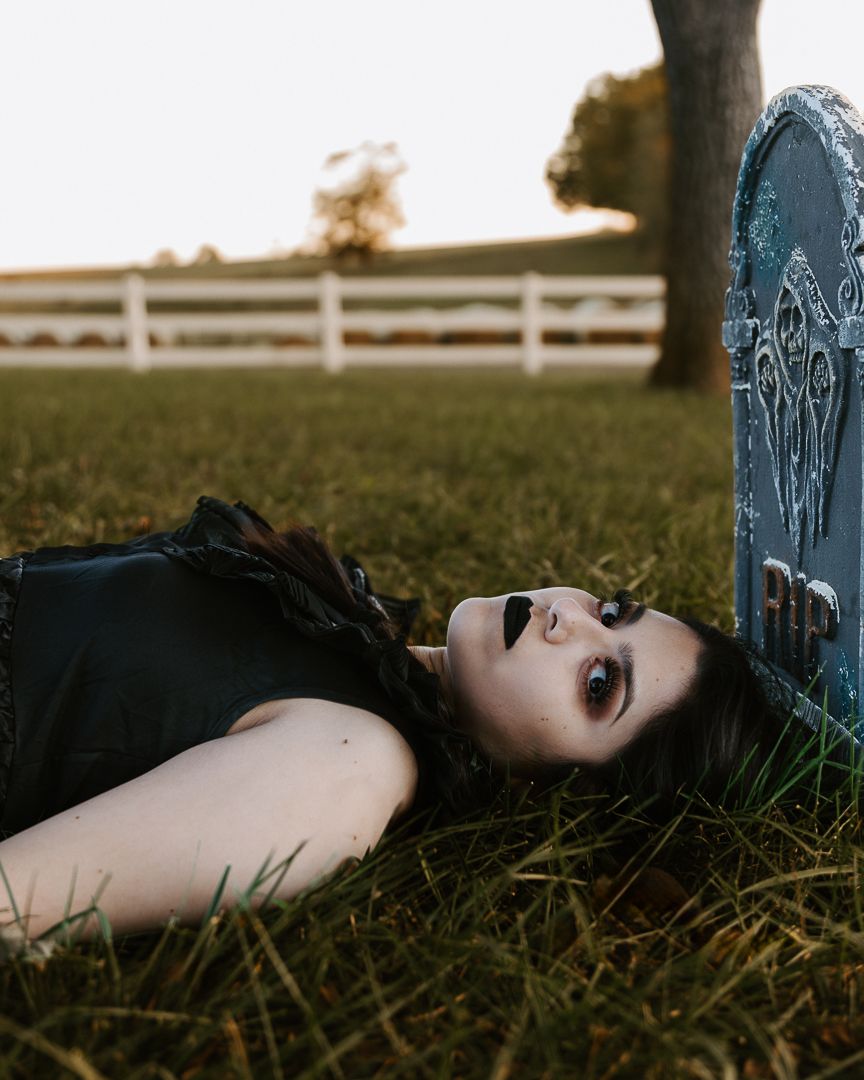 Artistic portrait showing someone lying in grass near a fence in dramatic lighting.