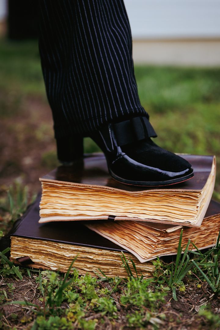 A sequence of close-up shots showing feet in pinstripe pants stepping on old weathered book pages in grass.