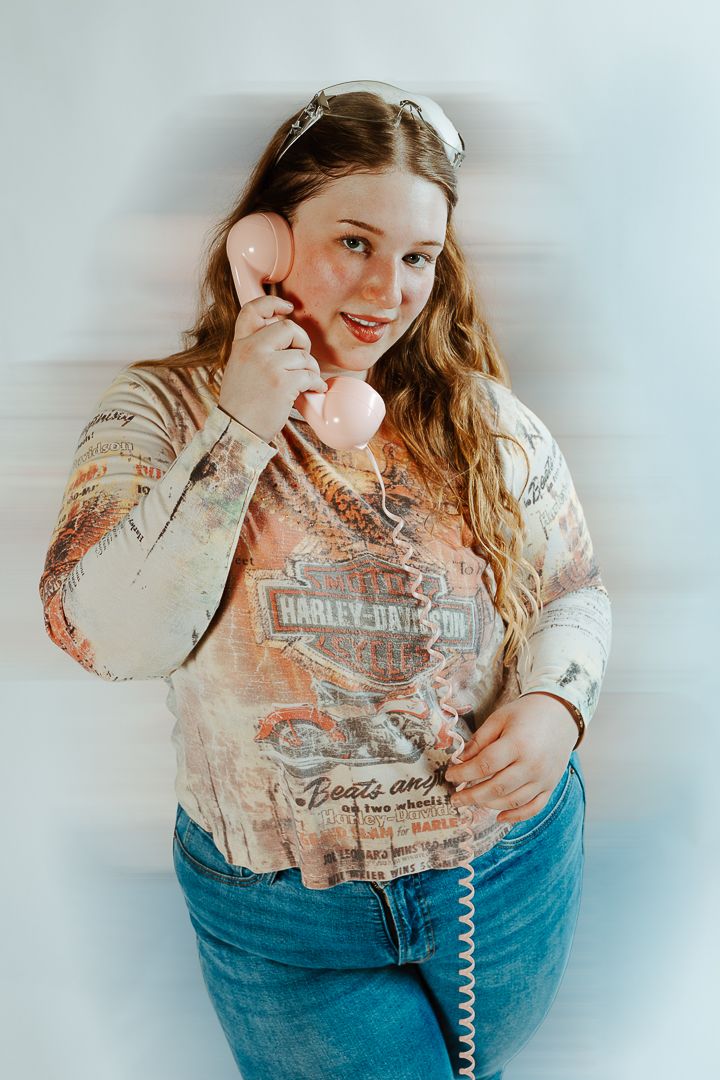 Person in white graphic tee and blue jeans posing playfully with retro telephone cord.