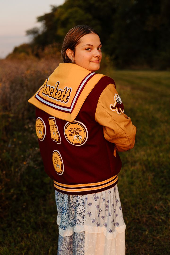 Varsity letterman jacket with patches shown over blue floral dress during golden hour photography.