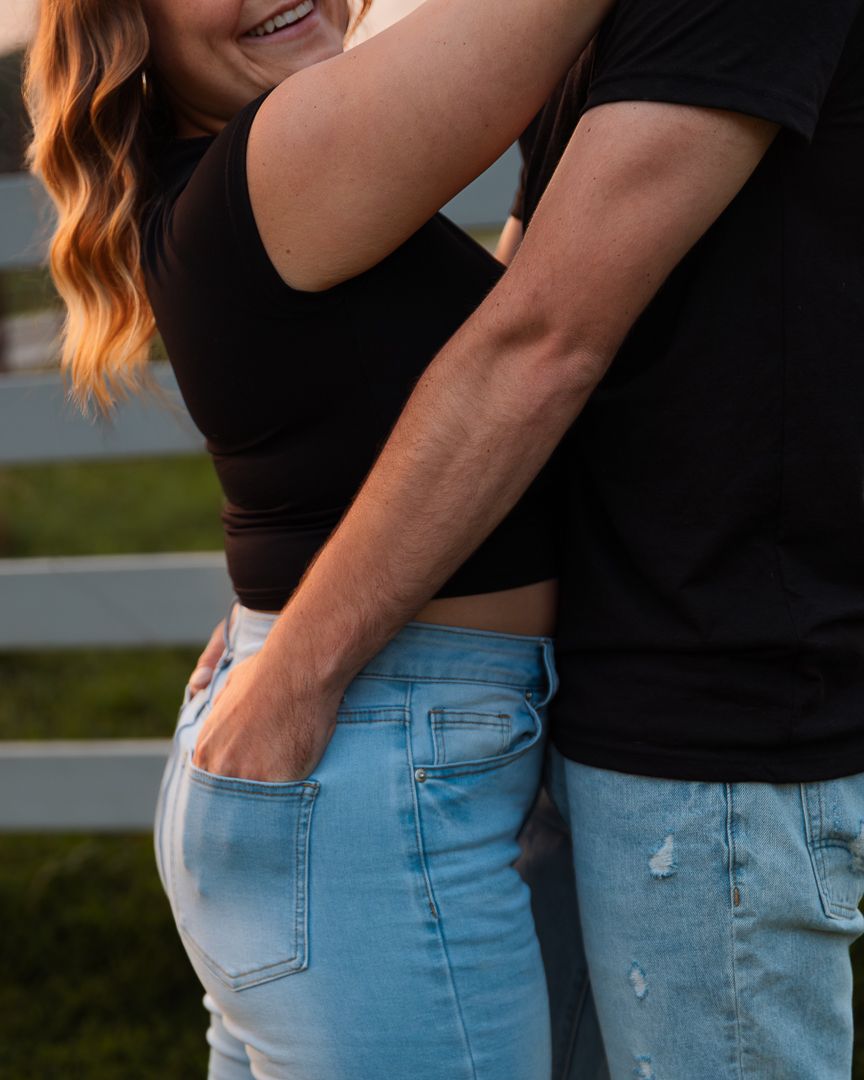 A couple embraces in casual outfits of black top and light denim during golden hour outdoors.